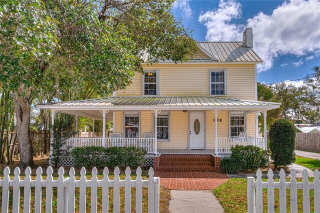 farmhouse featuring metal roof, a fenced front yard, a chimney, and a porch