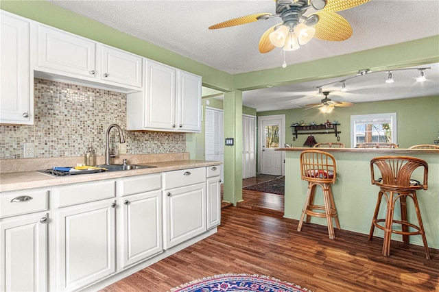 kitchen featuring dark wood-style floors, light countertops, backsplash, white cabinets, and a sink