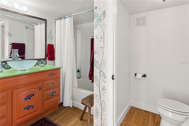 bathroom featuring toilet, wood finished floors, vanity, baseboards, and shower / bath combo