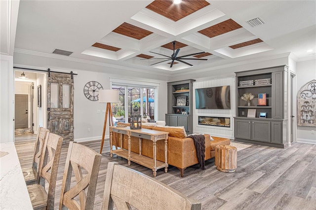 living room featuring ornamental molding, a barn door, light wood-style flooring, and visible vents