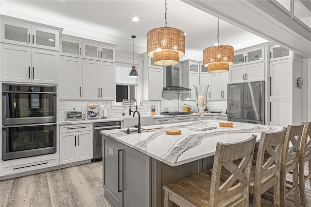 kitchen with an island with sink, wall chimney exhaust hood, appliances with stainless steel finishes, and a breakfast bar area