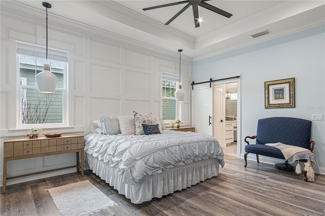 bedroom with dark wood-style flooring, visible vents, a decorative wall, a barn door, and ornamental molding