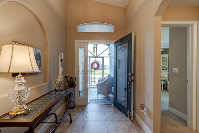 foyer featuring light tile patterned floors, arched walkways, and baseboards