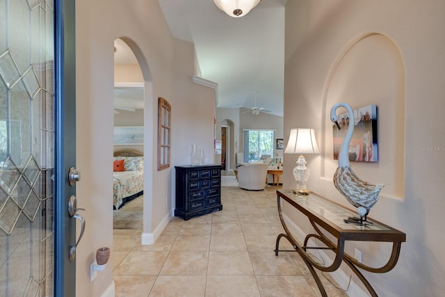 entrance foyer with arched walkways, a ceiling fan, light tile patterned flooring, vaulted ceiling, and baseboards