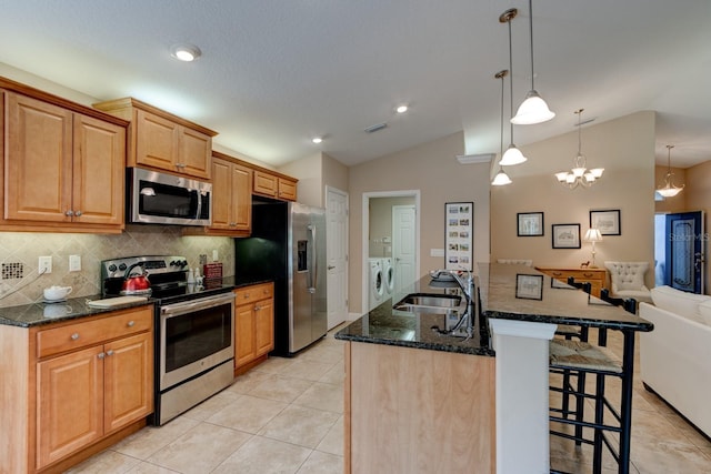 kitchen with a center island with sink, hanging light fixtures, appliances with stainless steel finishes, washing machine and dryer, and a sink