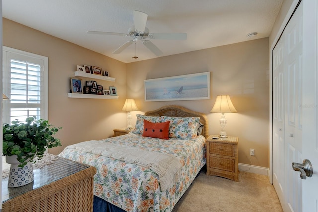 bedroom featuring light carpet, ceiling fan, baseboards, and a closet