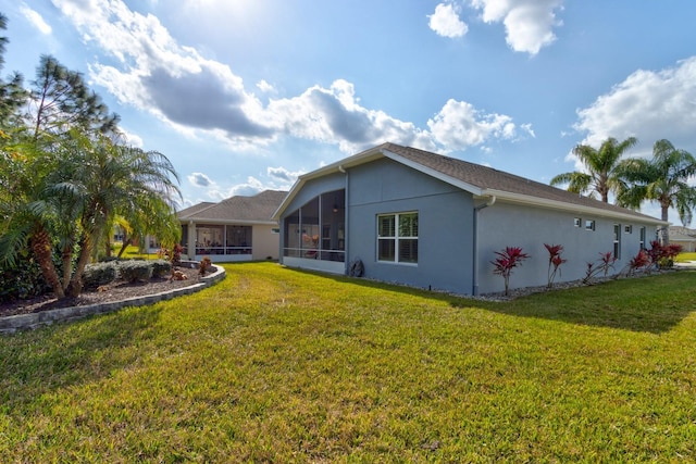 rear view of property featuring a sunroom, a lawn, and stucco siding