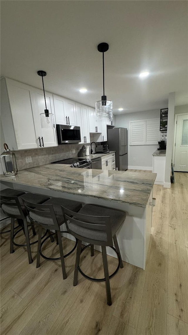 325 N Causeway Unit B101, New Smyrna Beach, FL 32169 - kitchen with stainless steel appliances, light wood-style floors, white cabinetry, light stone countertops, and decorative backsplash