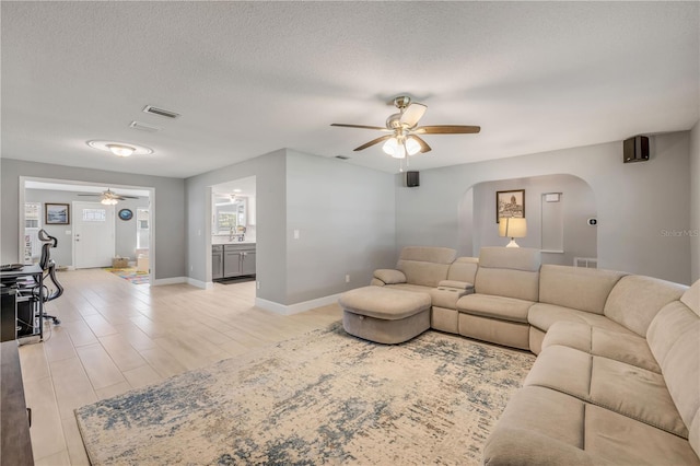 living room with ceiling fan, a textured ceiling, light wood-type flooring, and arched walkways