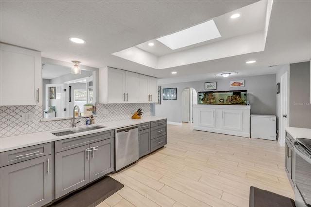 kitchen featuring appliances with stainless steel finishes, a tray ceiling, gray cabinets, light countertops, and a sink