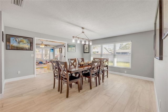 dining area with a textured ceiling, light wood finished floors, visible vents, and baseboards