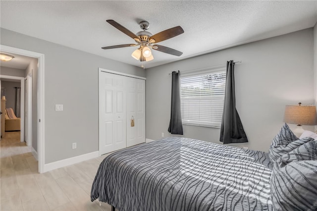 bedroom with baseboards, ceiling fan, light wood-style flooring, a textured ceiling, and a closet