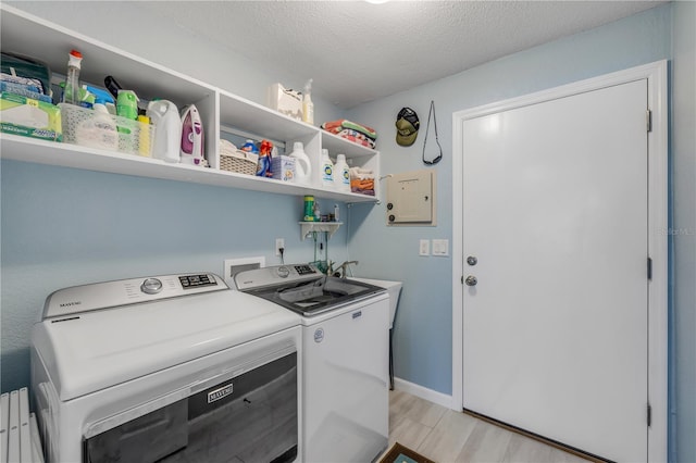 laundry area with laundry area, light wood-style flooring, a textured ceiling, and washing machine and clothes dryer