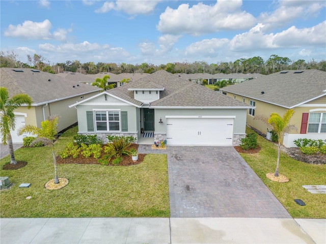 single story home featuring a garage, stone siding, decorative driveway, a residential view, and a front yard