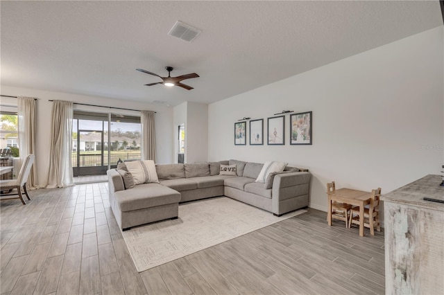 living area featuring a textured ceiling, a ceiling fan, visible vents, and wood tiled floor