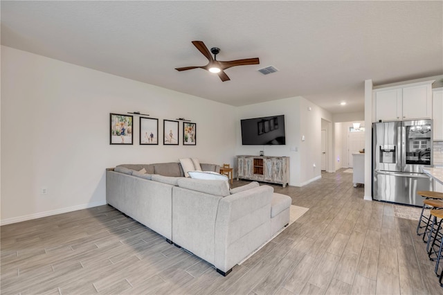 living area featuring ceiling fan, visible vents, light wood-style flooring, and baseboards