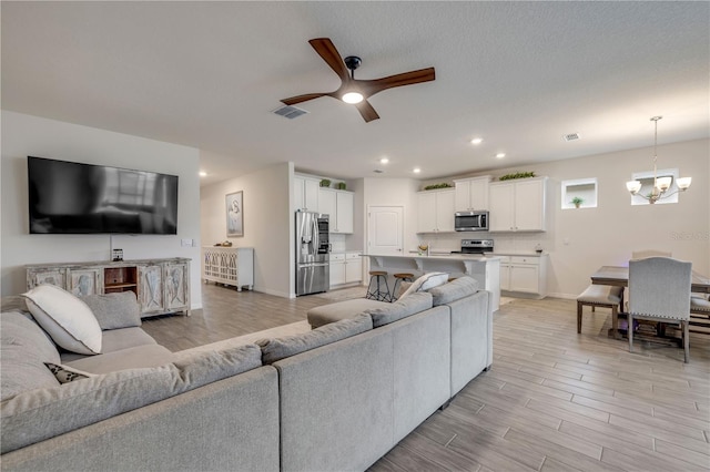 living area with recessed lighting, visible vents, light wood-style flooring, baseboards, and ceiling fan with notable chandelier