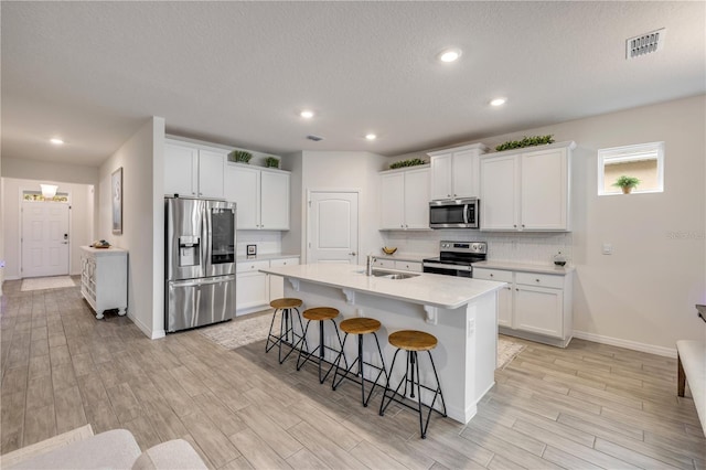 kitchen featuring visible vents, an island with sink, appliances with stainless steel finishes, light countertops, and a sink