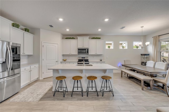 kitchen featuring light countertops, appliances with stainless steel finishes, an island with sink, and white cabinetry