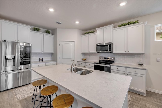 kitchen with a sink, white cabinetry, light countertops, appliances with stainless steel finishes, and an island with sink