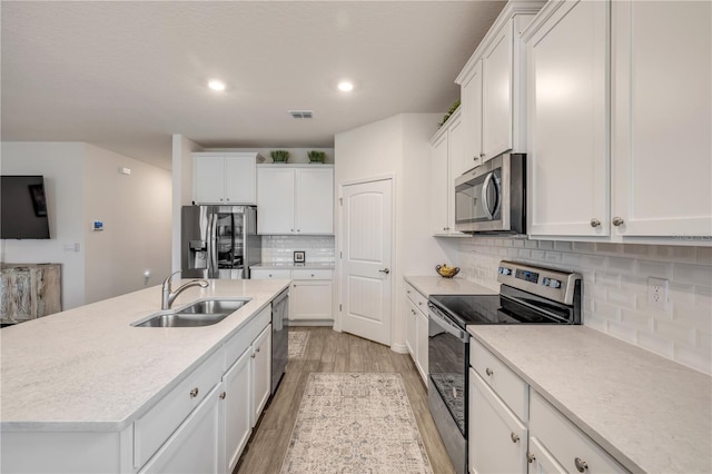 kitchen featuring an island with sink, appliances with stainless steel finishes, light countertops, white cabinetry, and a sink