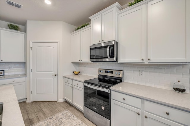 kitchen with light stone counters, stainless steel appliances, visible vents, light wood-style floors, and white cabinets