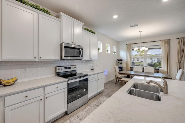 kitchen with stainless steel appliances, pendant lighting, white cabinets, and a sink