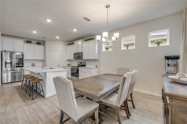 dining room with baseboards, light wood-type flooring, visible vents, and an inviting chandelier