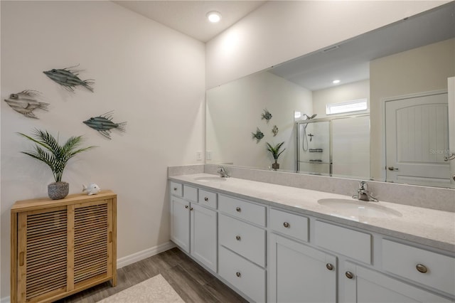 bathroom with double vanity, a shower stall, a sink, and wood finished floors