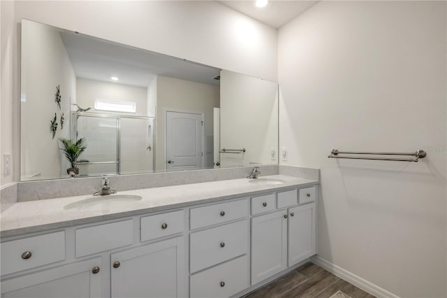 bathroom featuring double vanity, wood finished floors, a stall shower, and a sink