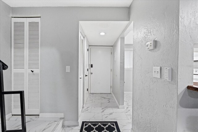 interior space featuring marble finish floor, baseboards, and a textured wall