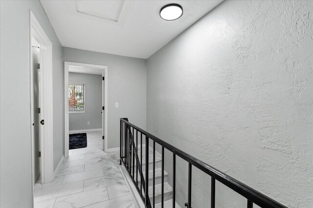 hallway with marble finish floor, a textured wall, and baseboards