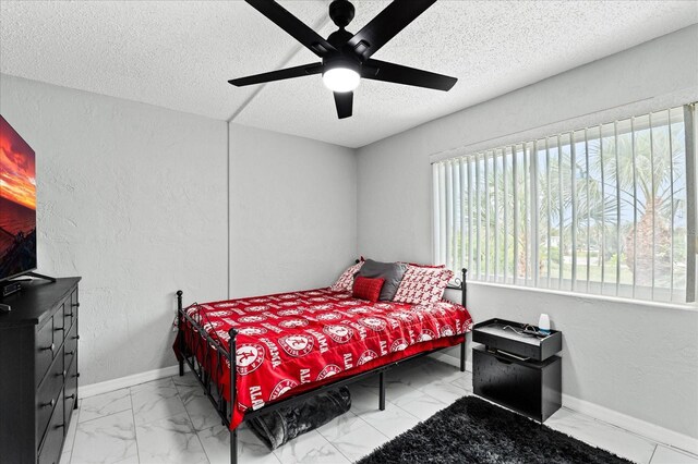 bedroom featuring baseboards, a ceiling fan, a textured wall, marble finish floor, and a textured ceiling