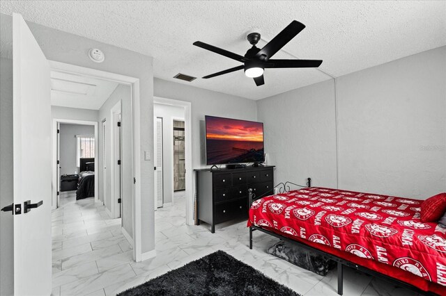 bedroom with a ceiling fan, marble finish floor, visible vents, and a textured ceiling