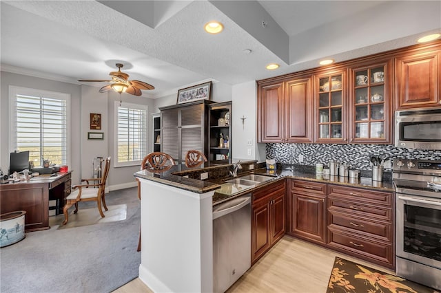 kitchen featuring stainless steel appliances, a sink, tasteful backsplash, dark stone countertops, and glass insert cabinets