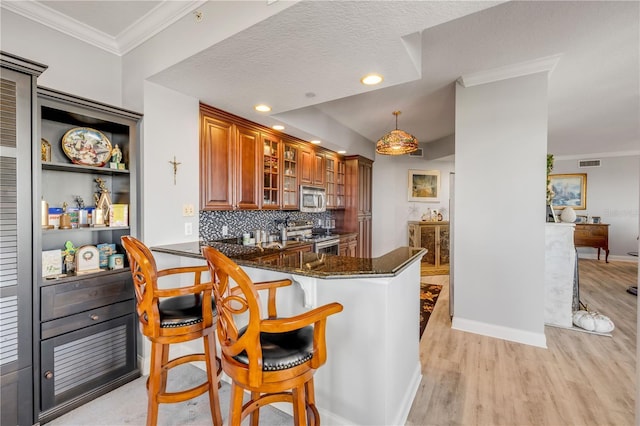 kitchen with dark stone counters, brown cabinetry, glass insert cabinets, a breakfast bar, and stainless steel appliances