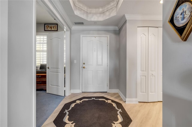 entryway featuring a raised ceiling, visible vents, ornamental molding, light wood-type flooring, and baseboards