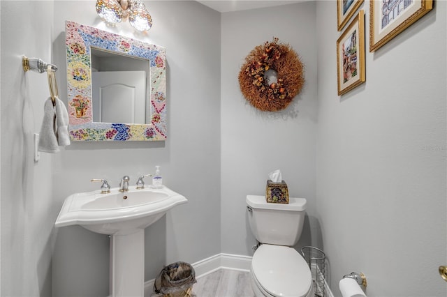 bathroom featuring toilet, a sink, baseboards, and wood finished floors