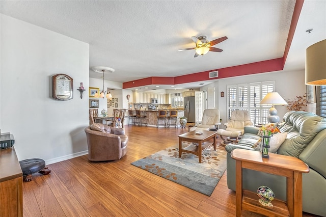 living area with visible vents, a textured ceiling, wood finished floors, baseboards, and ceiling fan with notable chandelier