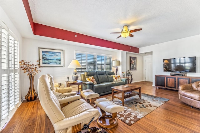 living area featuring a textured ceiling, wood finished floors, a ceiling fan, and baseboards