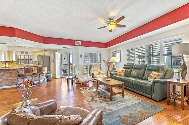 living room with hardwood / wood-style flooring, ceiling fan, visible vents, and a textured ceiling