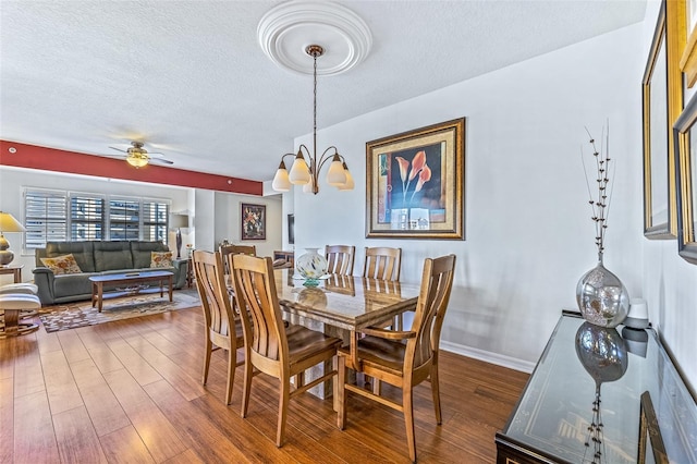 dining room featuring a textured ceiling, ceiling fan with notable chandelier, wood finished floors, and baseboards