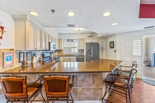 kitchen with cream cabinets, a peninsula, wood finished floors, visible vents, and appliances with stainless steel finishes