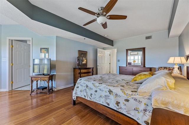 bedroom with ceiling fan, wood finished floors, visible vents, and baseboards