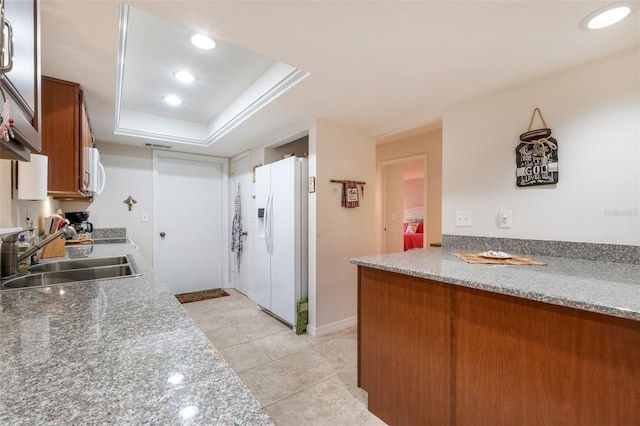 kitchen with a raised ceiling, brown cabinets, white fridge with ice dispenser, a sink, and light tile patterned flooring