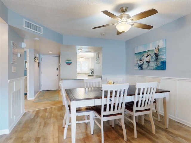 dining area featuring light wood-style floors, visible vents, a textured ceiling, and wainscoting