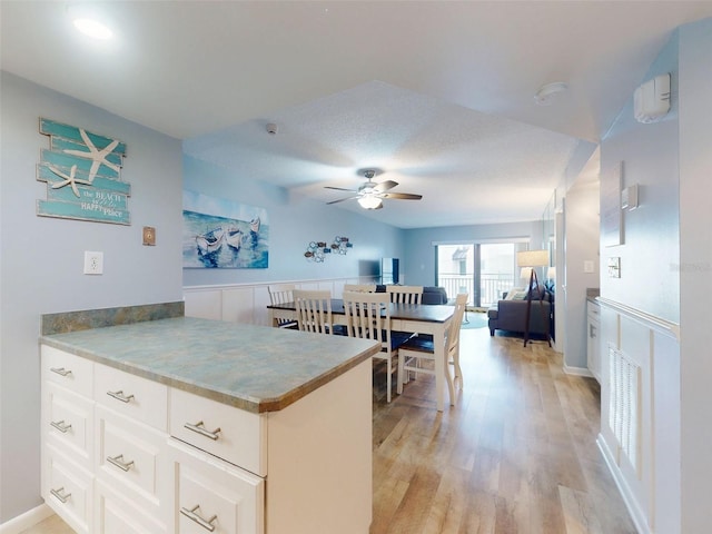 kitchen with a peninsula, a ceiling fan, white cabinets, open floor plan, and light wood-type flooring