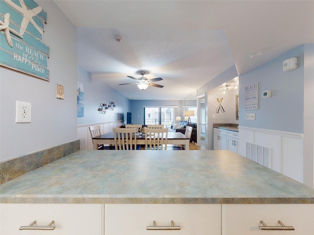 kitchen with a textured ceiling, ceiling fan, visible vents, white cabinets, and open floor plan