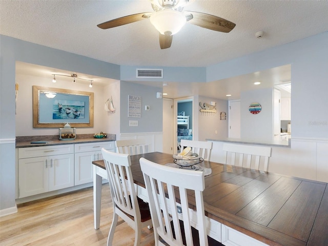 dining area with a textured ceiling, ceiling fan, visible vents, wainscoting, and light wood finished floors