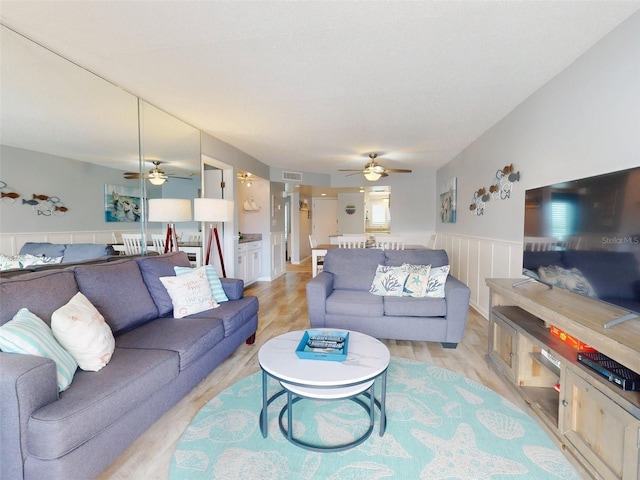 living area with light wood-type flooring, a wainscoted wall, visible vents, and a ceiling fan